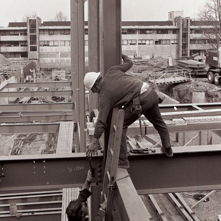 Black and white photo of workers climbing a ladder on the Center Building during its construction.