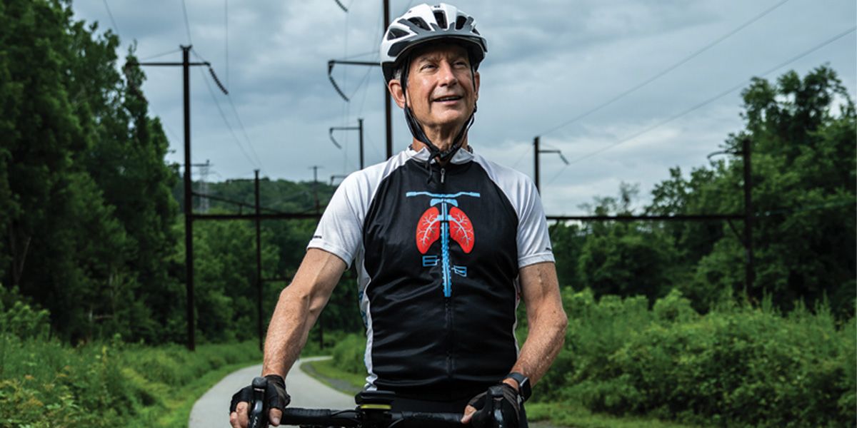 John Matthews dressed in athletic attire and wearing a bike helmet stops for a photo while riding his bike.