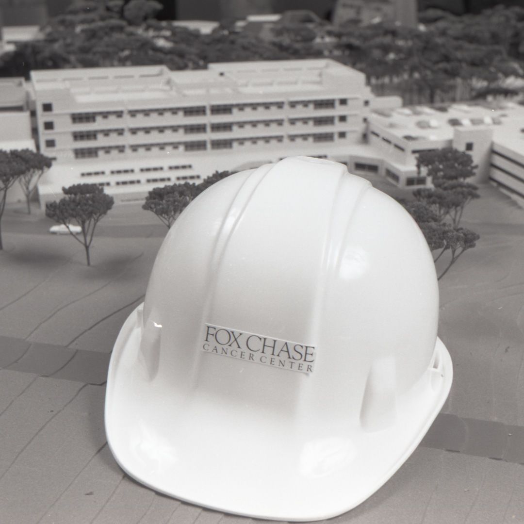 Black and white photo of a hard hat beside a miniature model of  Fox Chase Cancer Center.